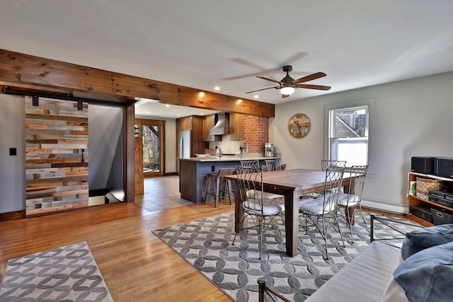 dining area featuring wood walls, ceiling fan, light hardwood / wood-style floors, and a baseboard radiator