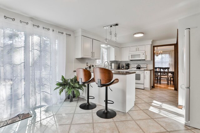 kitchen with kitchen peninsula, a wealth of natural light, white cabinets, and white appliances