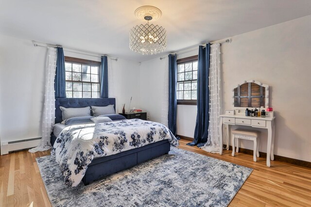 bedroom featuring an inviting chandelier, light hardwood / wood-style flooring, a baseboard radiator, and multiple windows