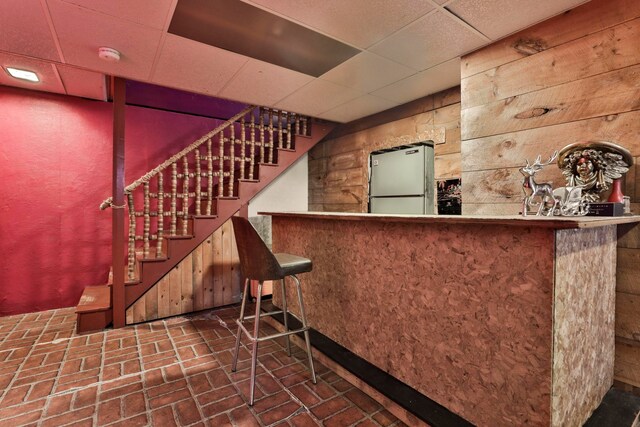 bar with a drop ceiling, stainless steel fridge, and wooden walls