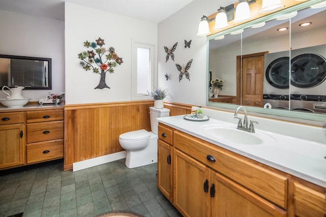 bathroom with vanity, wood walls, toilet, and stacked washer / dryer