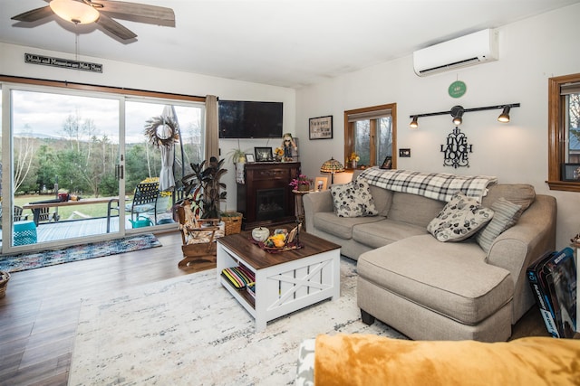 living room featuring hardwood / wood-style floors, a wall mounted AC, a healthy amount of sunlight, and ceiling fan