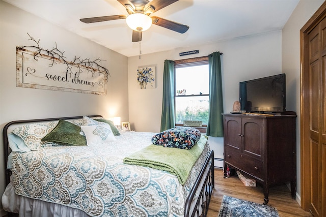 bedroom with hardwood / wood-style flooring, ceiling fan, baseboard heating, and a closet