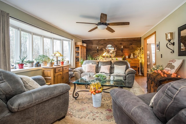 living room with ceiling fan, wood walls, and ornamental molding