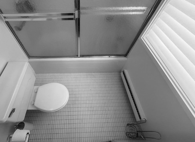 bathroom featuring tile patterned floors, bath / shower combo with glass door, a baseboard radiator, and toilet