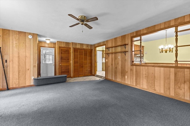 carpeted spare room featuring wooden walls and ceiling fan with notable chandelier