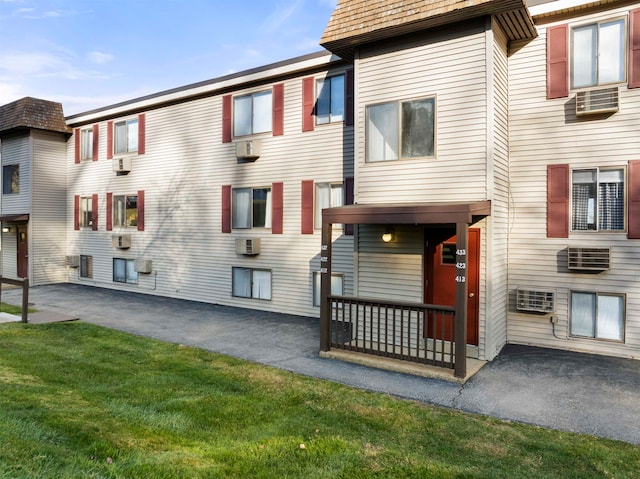 view of front of home featuring a wall mounted air conditioner and a front lawn