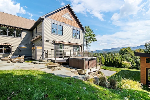 rear view of house featuring a patio area, a mountain view, a yard, and a hot tub