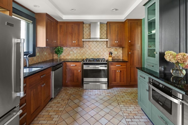 kitchen with appliances with stainless steel finishes, backsplash, dark stone counters, sink, and wall chimney range hood