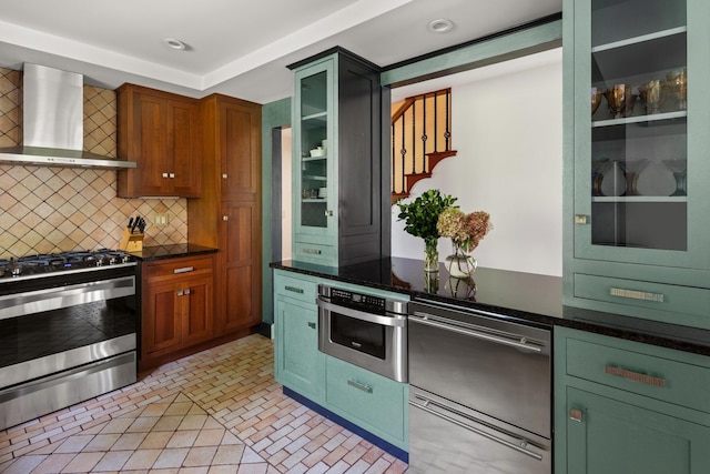 kitchen featuring backsplash, wall chimney exhaust hood, dark stone counters, and appliances with stainless steel finishes