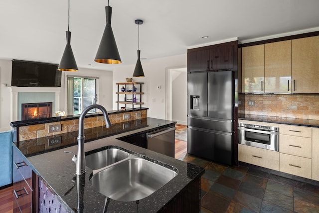 kitchen with pendant lighting, dark stone counters, a center island with sink, sink, and stainless steel appliances