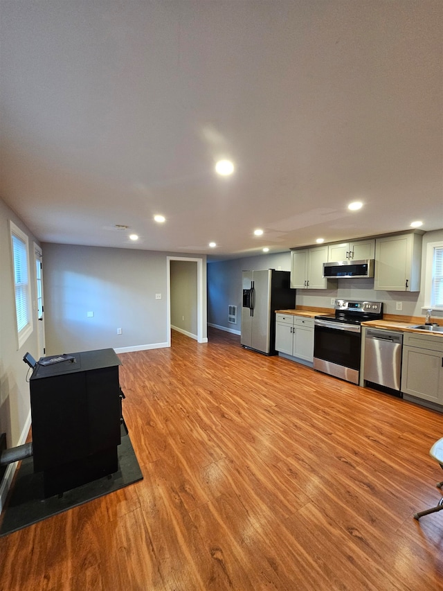 kitchen with exhaust hood, green cabinets, sink, appliances with stainless steel finishes, and light hardwood / wood-style floors