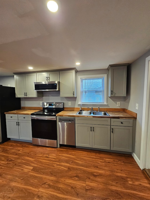 kitchen featuring butcher block counters, sink, extractor fan, appliances with stainless steel finishes, and hardwood / wood-style flooring