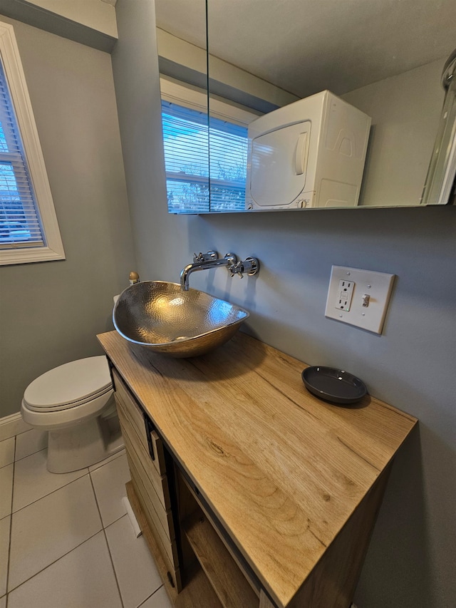 bathroom featuring toilet, stacked washer and dryer, vanity, and tile patterned flooring