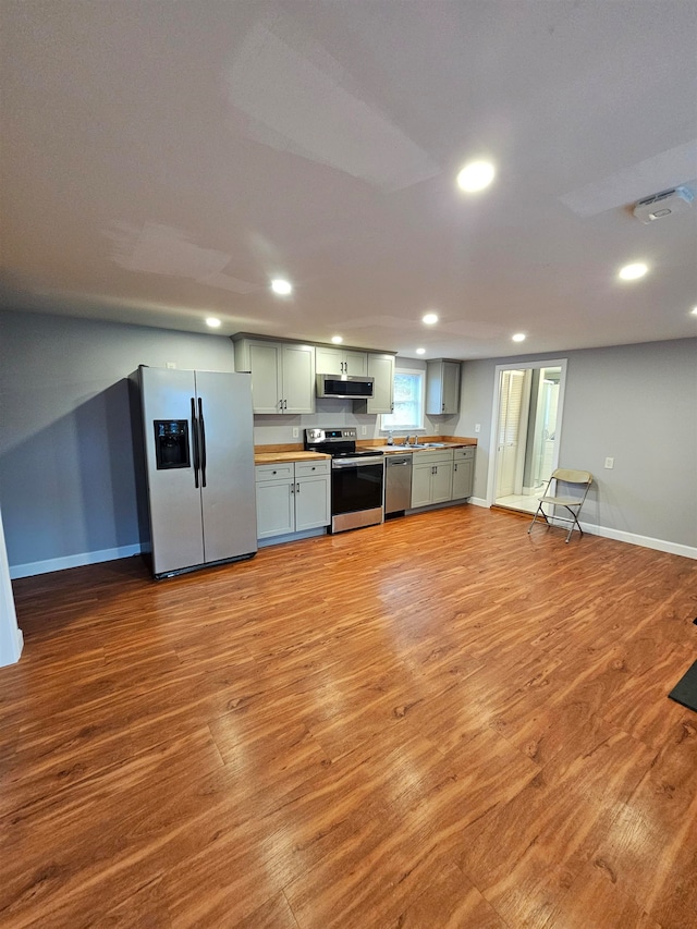 kitchen with wood counters, exhaust hood, green cabinets, light hardwood / wood-style flooring, and stainless steel appliances