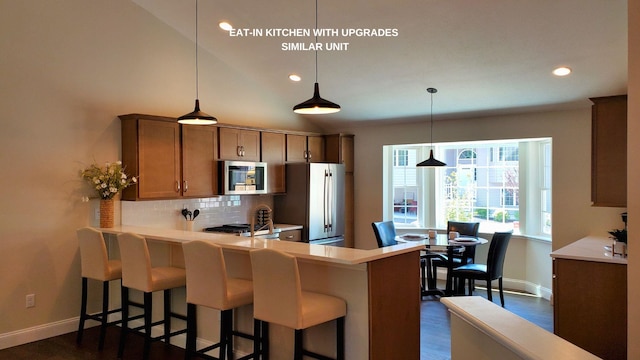 kitchen featuring a breakfast bar area, appliances with stainless steel finishes, hanging light fixtures, kitchen peninsula, and tasteful backsplash