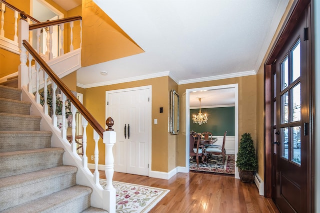 entrance foyer with hardwood / wood-style flooring, a notable chandelier, crown molding, and a baseboard heating unit