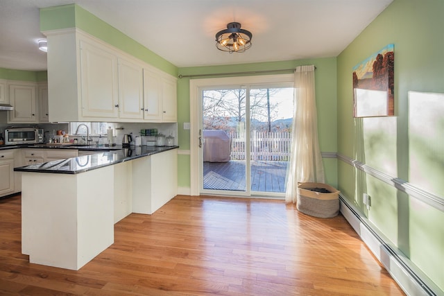 kitchen with white cabinetry, sink, baseboard heating, kitchen peninsula, and light hardwood / wood-style floors