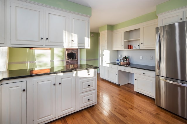 kitchen with light hardwood / wood-style flooring, kitchen peninsula, stainless steel fridge, white cabinets, and built in desk