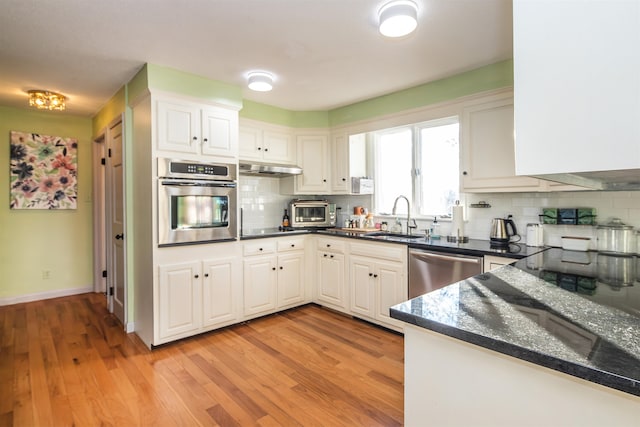 kitchen with tasteful backsplash, stainless steel appliances, sink, white cabinets, and light hardwood / wood-style floors