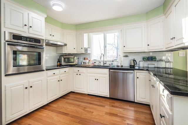 kitchen with sink, stainless steel appliances, backsplash, white cabinets, and light wood-type flooring