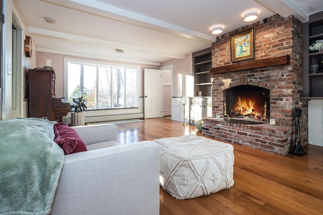 living room with built in shelves, a baseboard radiator, a brick fireplace, beamed ceiling, and hardwood / wood-style floors