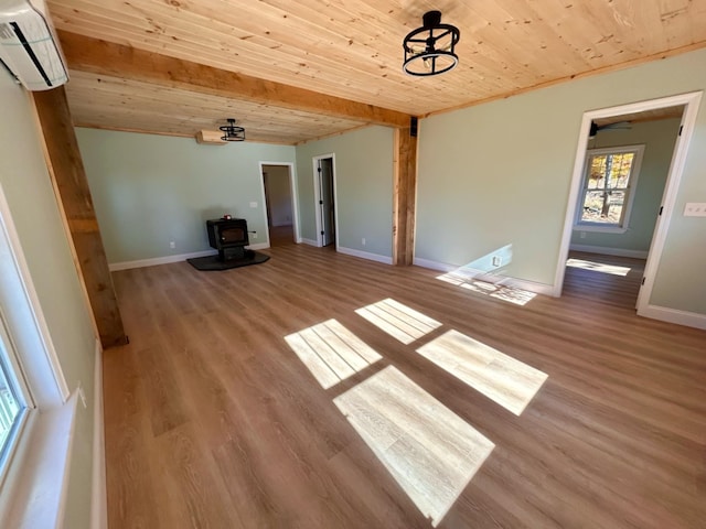 unfurnished living room featuring a wood stove, beamed ceiling, a wall unit AC, light hardwood / wood-style floors, and wood ceiling