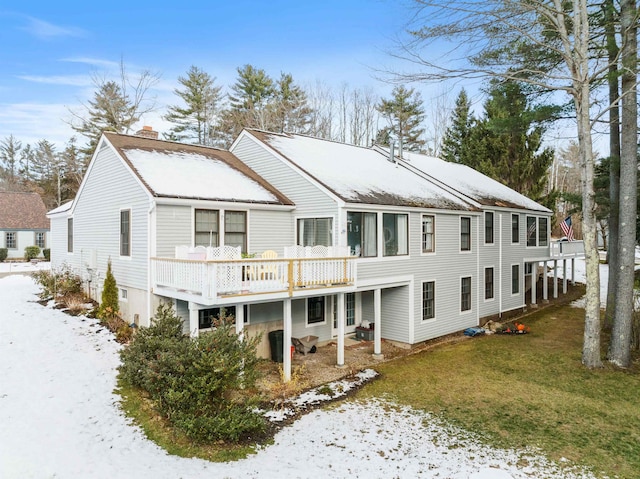 snow covered rear of property with a deck and a lawn