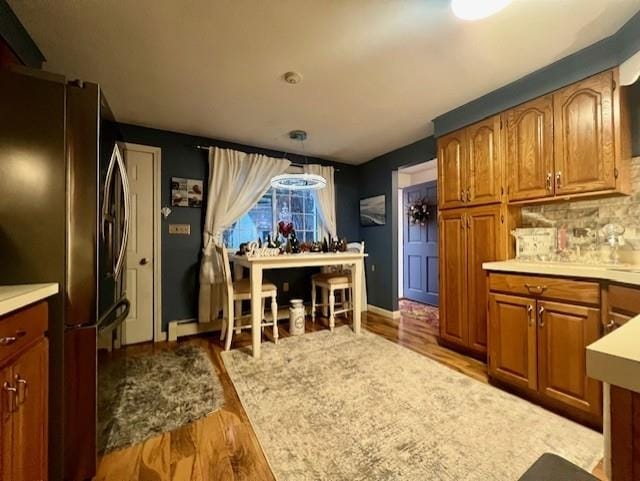 kitchen featuring stainless steel fridge, light wood-type flooring, hanging light fixtures, and tasteful backsplash