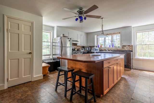 kitchen with white cabinetry, ceiling fan, stainless steel fridge, decorative backsplash, and a kitchen island