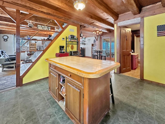 kitchen featuring tile counters, a center island, beam ceiling, and a breakfast bar area