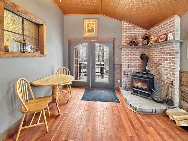 entryway featuring hardwood / wood-style flooring, a wood stove, ornamental molding, and vaulted ceiling