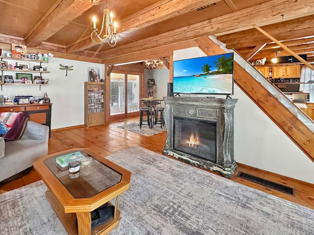 living room featuring beamed ceiling, wooden ceiling, light wood-type flooring, and a chandelier