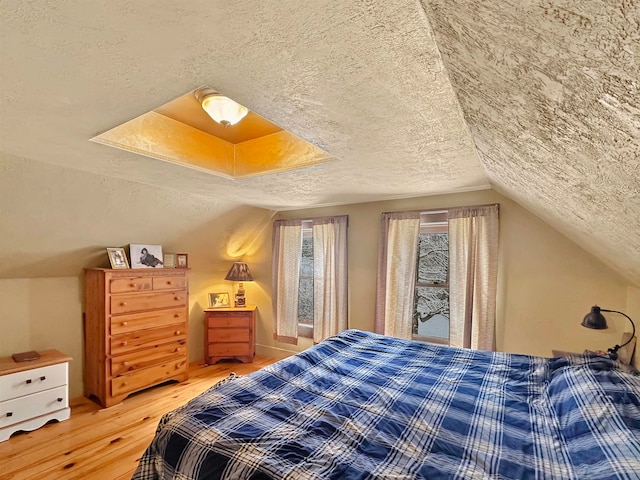 bedroom with a textured ceiling, hardwood / wood-style flooring, and vaulted ceiling