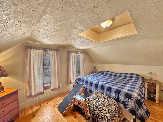 bedroom with wood-type flooring, a textured ceiling, and vaulted ceiling