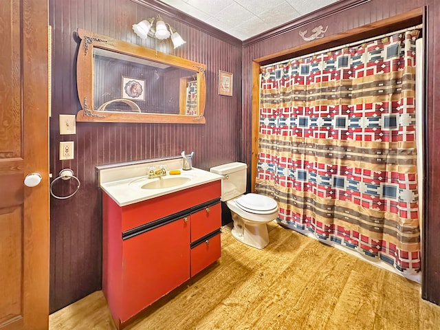 bathroom with crown molding, wood-type flooring, toilet, wooden walls, and vanity