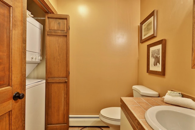 bathroom featuring stacked washing maching and dryer, tile patterned floors, vanity, baseboard heating, and toilet