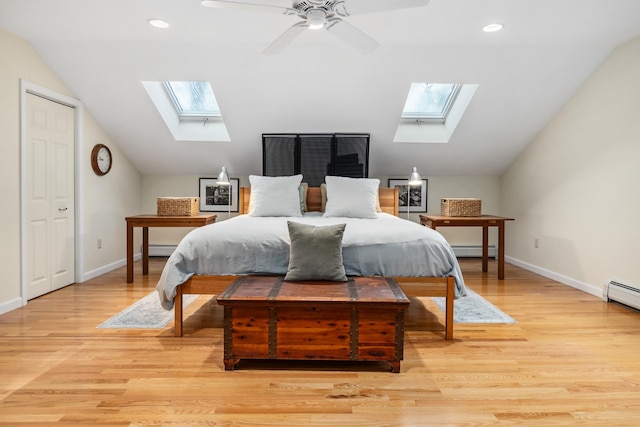 bedroom featuring a baseboard radiator, light hardwood / wood-style flooring, ceiling fan, and vaulted ceiling with skylight