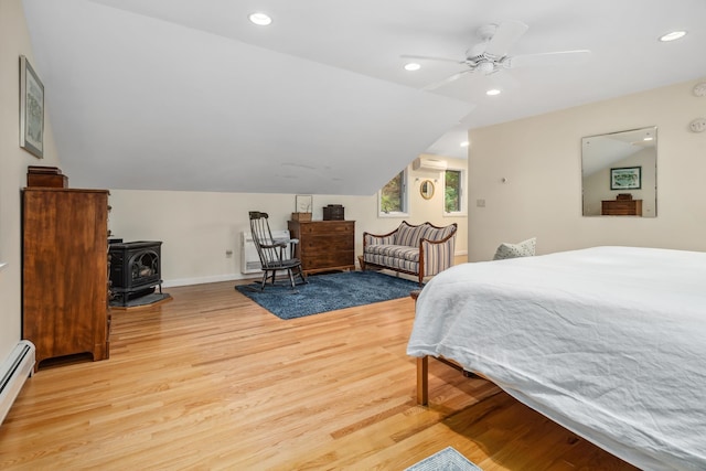 bedroom featuring ceiling fan, light wood-type flooring, a wood stove, and vaulted ceiling