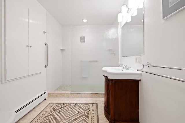 bathroom with tiled shower, vanity, and a baseboard heating unit