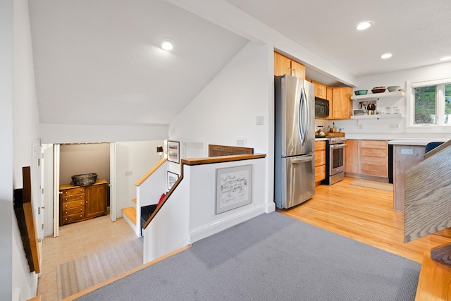 kitchen featuring appliances with stainless steel finishes, light brown cabinetry, light hardwood / wood-style floors, and lofted ceiling