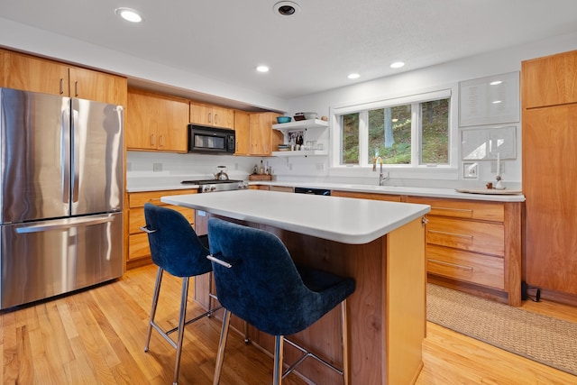 kitchen with stainless steel refrigerator, a center island, sink, light hardwood / wood-style floors, and a breakfast bar