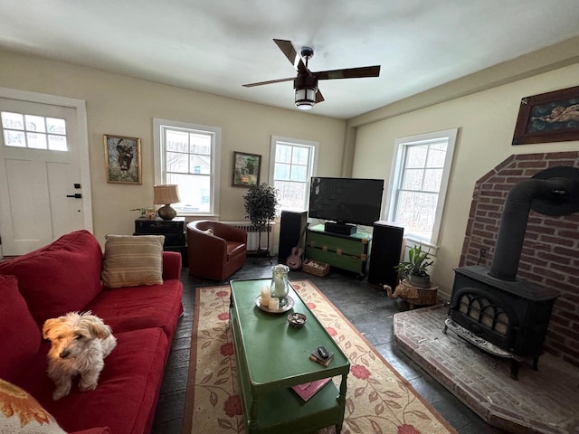 living room featuring a wood stove, ceiling fan, and a healthy amount of sunlight