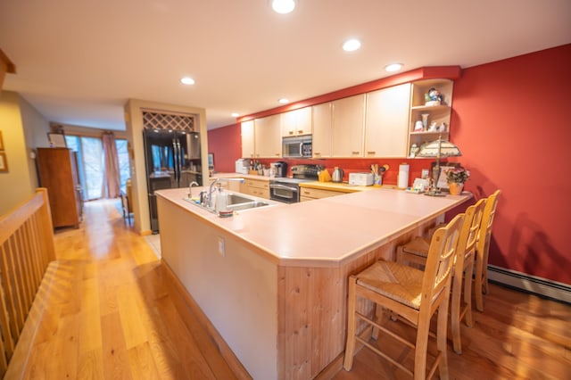 kitchen with kitchen peninsula, stainless steel appliances, sink, light hardwood / wood-style floors, and a breakfast bar area