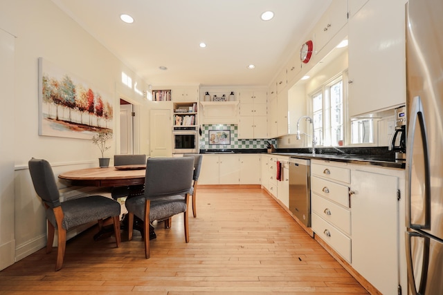 kitchen with tasteful backsplash, white cabinetry, appliances with stainless steel finishes, and light hardwood / wood-style flooring