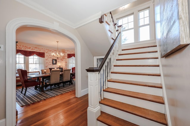 staircase featuring hardwood / wood-style flooring, crown molding, and an inviting chandelier