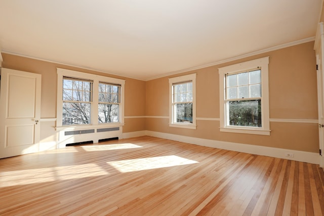 empty room with ornamental molding, radiator, and light hardwood / wood-style floors