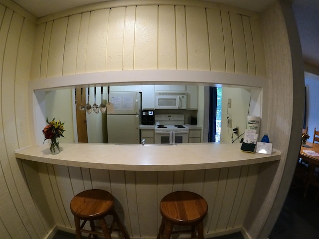 kitchen with white appliances, a peninsula, and wood walls