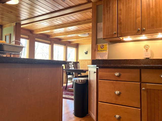 kitchen featuring beam ceiling, light hardwood / wood-style flooring, dark stone counters, and wood ceiling