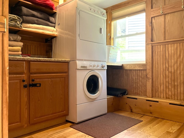 laundry area with stacked washer / dryer, light hardwood / wood-style flooring, and cabinets